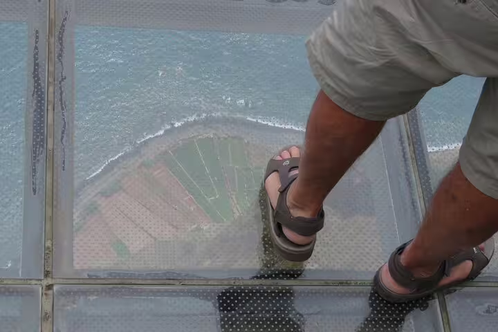 Person standing on Madeira's glass skywalk, overlooking the ocean, during a thrilling 4x4 adventure with wine and tapas.