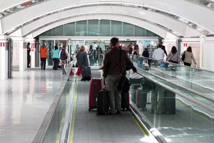 Travelers with luggage on moving walkway at Madrid Atocha, private transfer to city center hotels