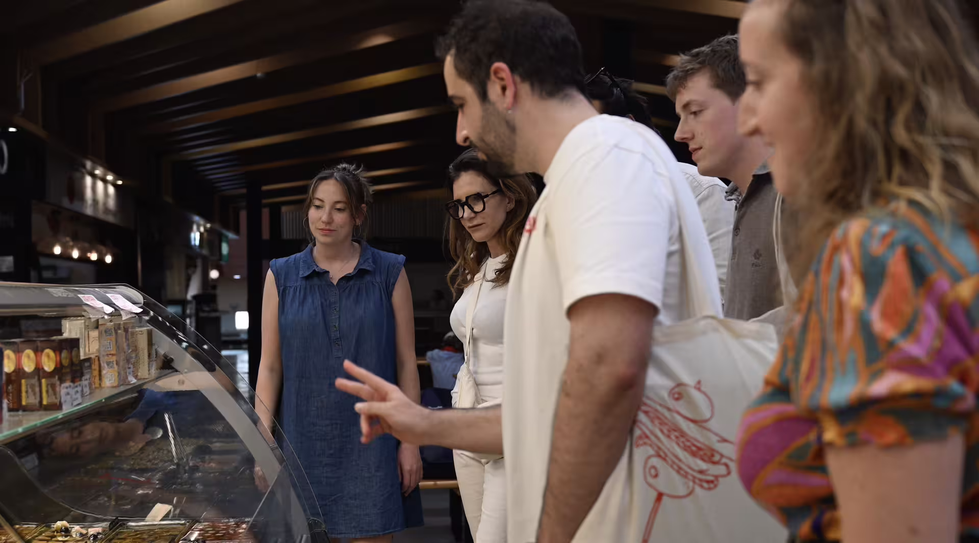 Tourists explore local delicacies at a vibrant Madrid market during an Authentic Food, Wine & Culture experience.
