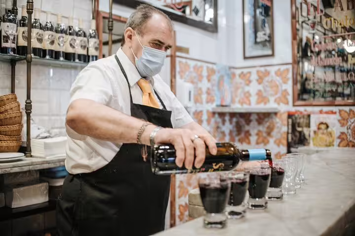A masked bartender pours red wine in a traditional Madrid tapas bar, showcasing authentic Spanish culinary culture.