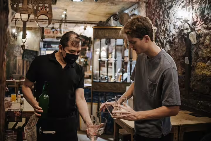 A local guide assists a tourist with traditional cider pouring during a vibrant tapas tour in a cozy Madrid tavern.