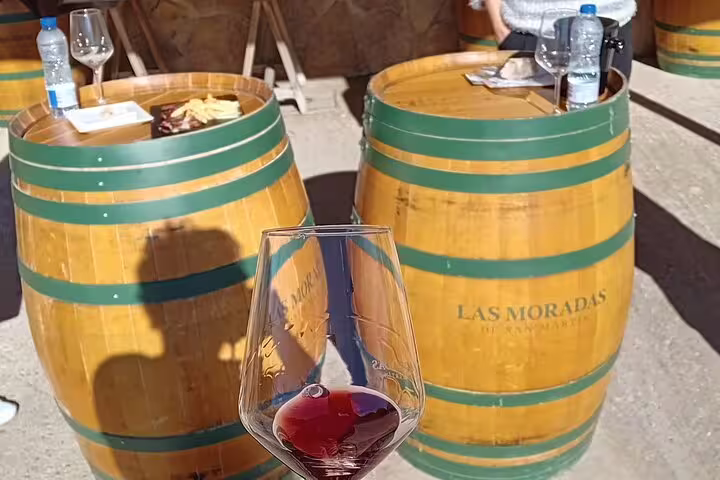 Close-up of a wine glass with red wine, set against wooden barrels at Las Moradas winery in Madrid.