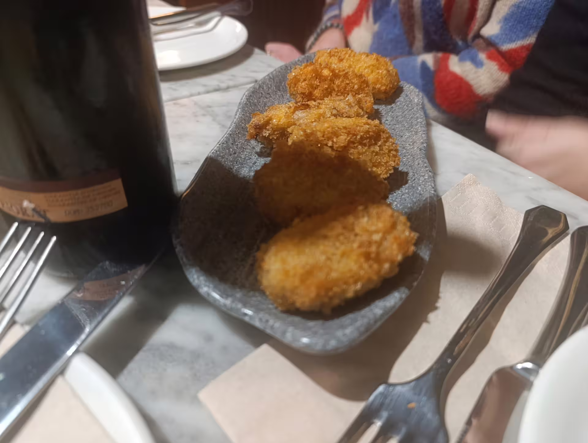 Close-up of golden croquetas and a wine bottle on a Madrid wine tasting tour table setting.