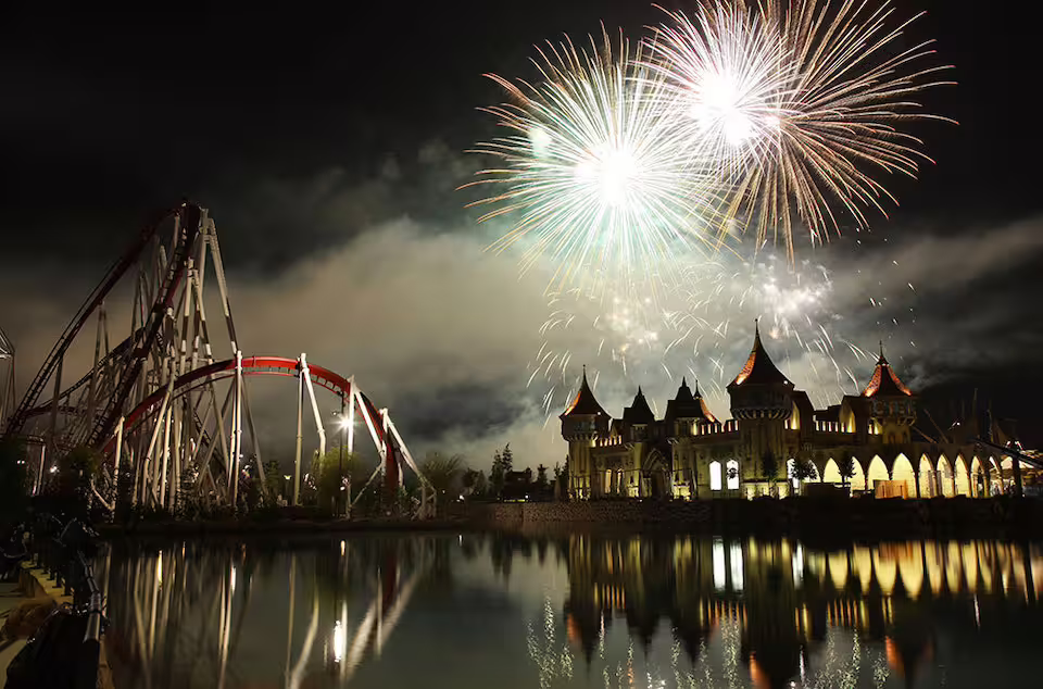 Night fireworks over MagicLand Amusement Park castle and roller coaster, highlighting the park entrance experience