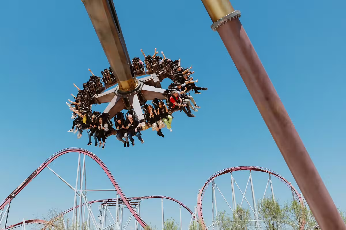 Thrill ride spinning high above MagicLand Amusement Park with riders and roller coaster track below