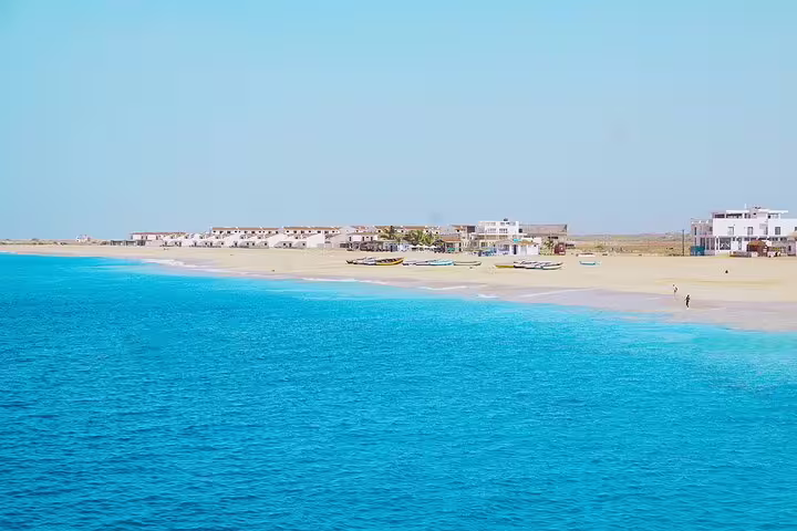 Pristine sandy beach with turquoise waters and boats along the shore in Vila do Maio, perfect for relaxation.