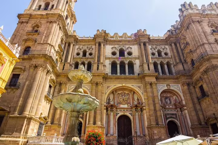 Stunning view of Malaga Cathedral's intricate facade and ornate fountain under a clear blue sky.