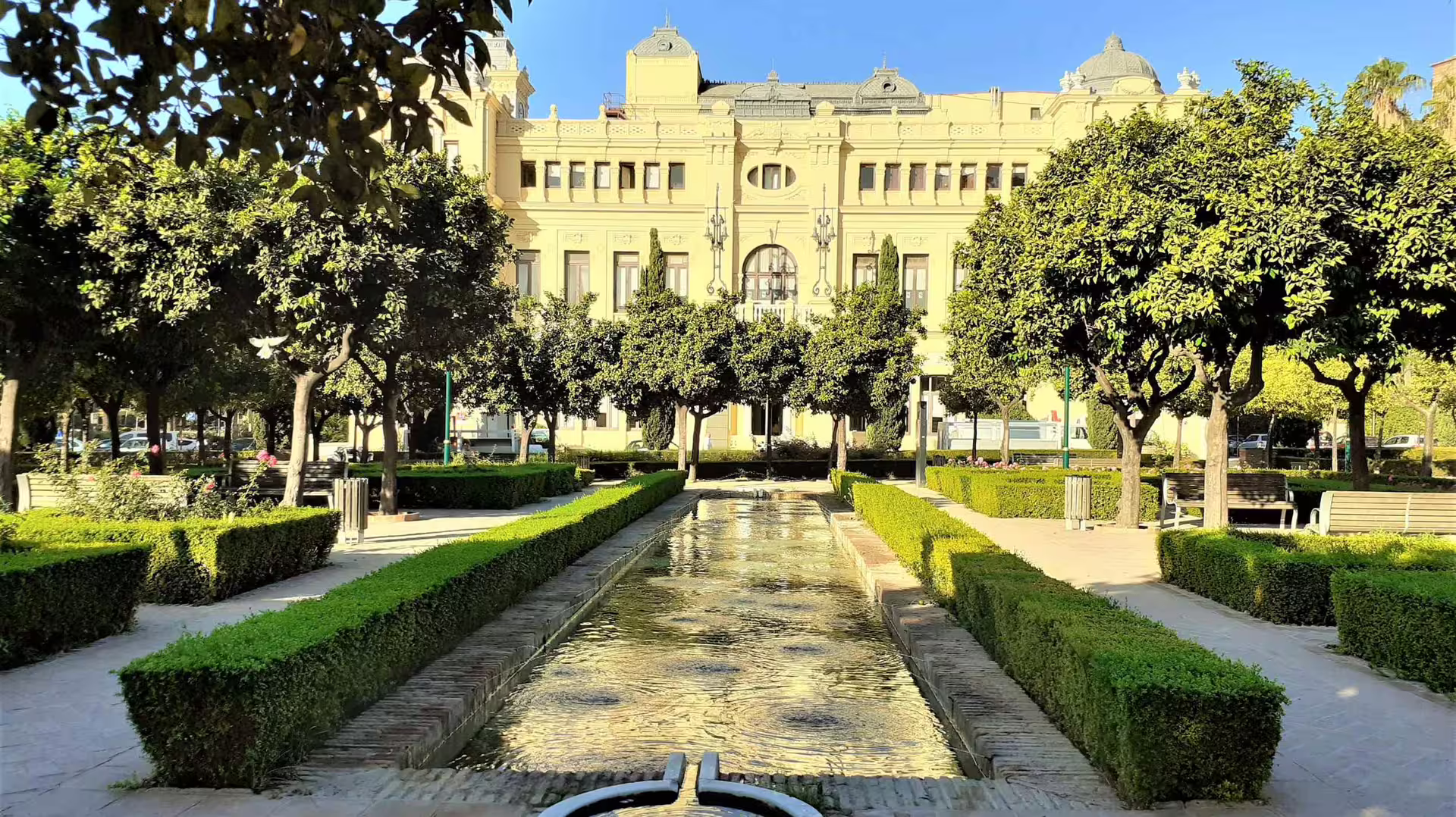 Malaga city park with reflecting canal and historic building, stop on private tour from Marbella