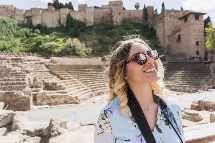 Smiling tourist enjoys the ancient Roman Theatre with the historic Alcazaba of Malaga in the background.