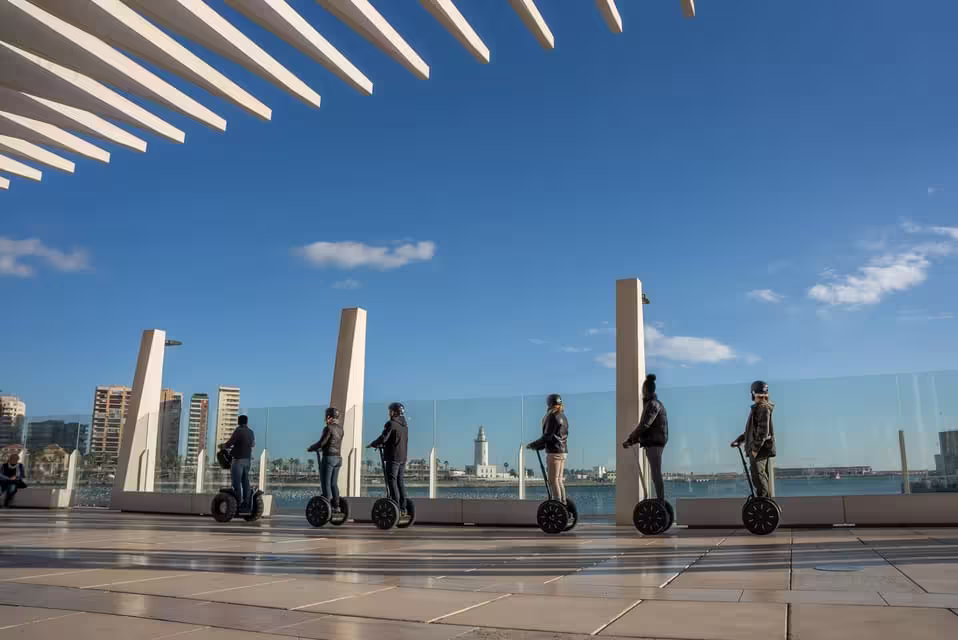 Tourists on Segways exploring Malaga's modern architecture and harbor views on a sunny day city tour.