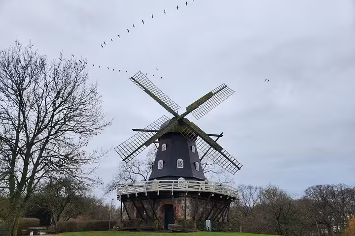 Historic Dutch windmill surrounded by trees under a cloudy sky in Malmö, Sweden, ideal for cultural exploration tours.