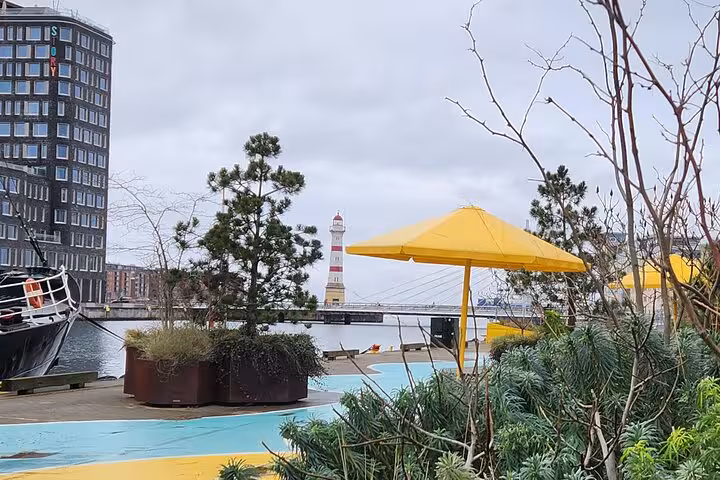 Lively waterfront scene in Malmö with yellow umbrellas, lush greenery, and iconic lighthouse on a guided highlight tour.