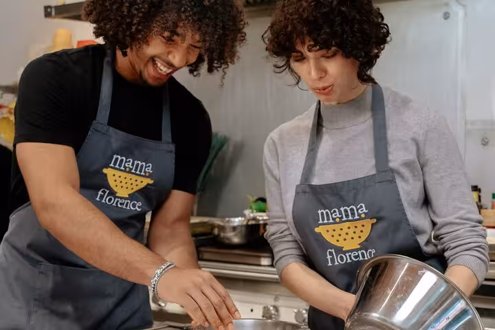 Two participants engaging in a hands-on cooking experience at MaMa Florence, smiling as they prepare a Tuscan dish.