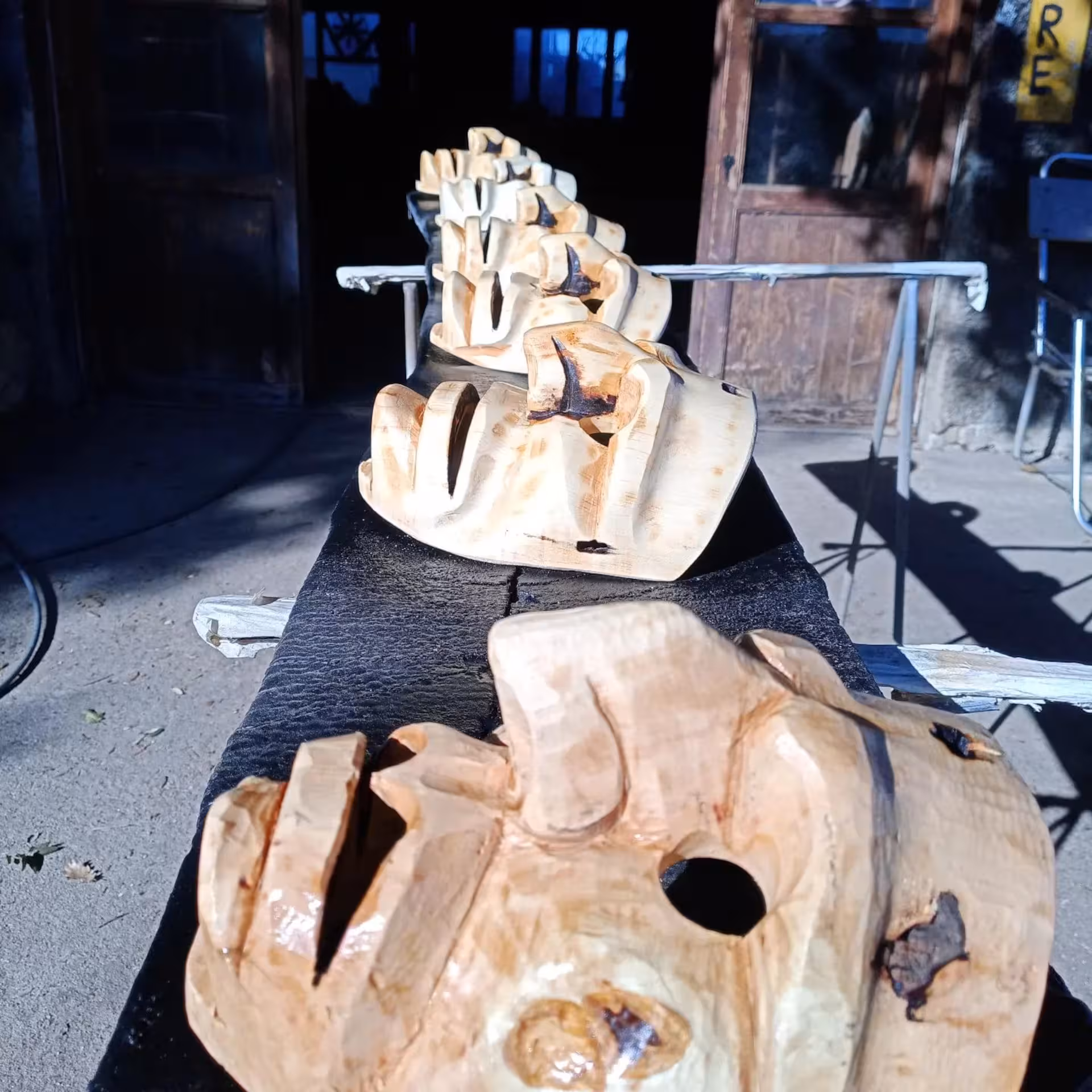 Row of unfinished wooden Sardinian masks drying in the sun outside a Mamoiada workshop.