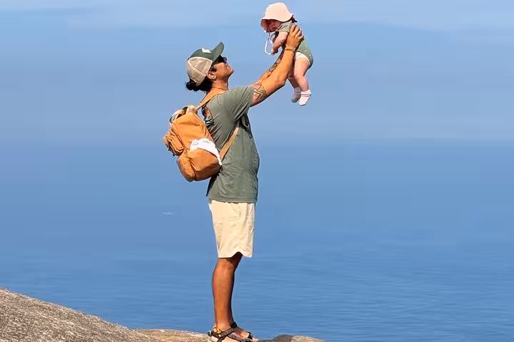 Man holding a baby aloft on a scenic trail in DA Tijuca Forest with expansive ocean views.