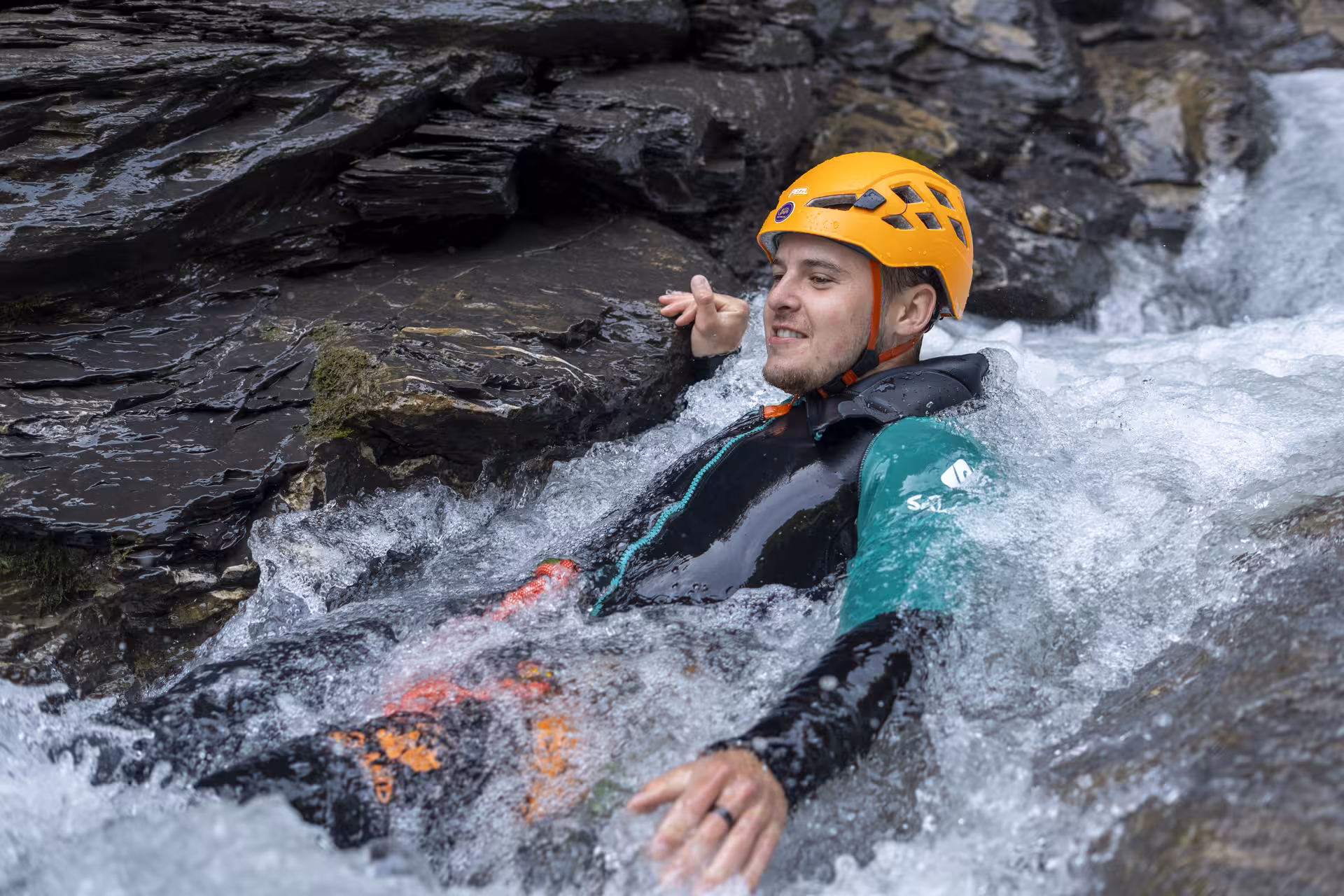 Man in helmet enjoys sliding through a natural water chute during Interlaken canyoning adventure.