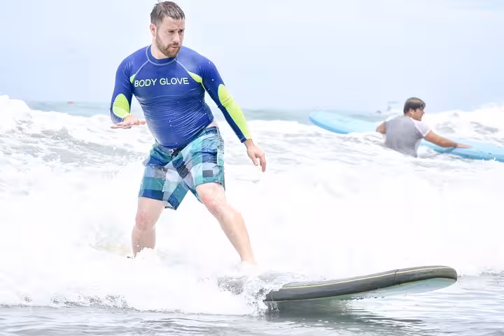 Man catching a wave during surf lesson in Manuel Antonio, showcasing skill and balance on a sunny day.
