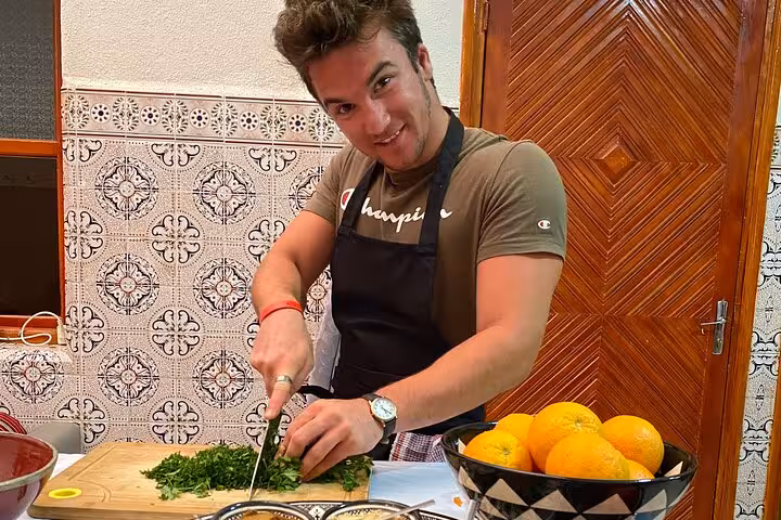 Man in kitchen apron chopping fresh herbs for a cooking class at parents place with oranges in a traditional setting.