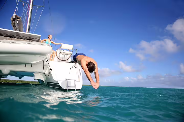 Man diving off a private catamaran in clear turquoise waters during a full-day Ibiza and Formentera trip, under a sunny sky.