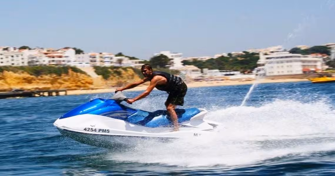 Man enjoying a thrilling ride on a jet ski in crystal blue waters near a coastal town, perfect for adventure seekers.