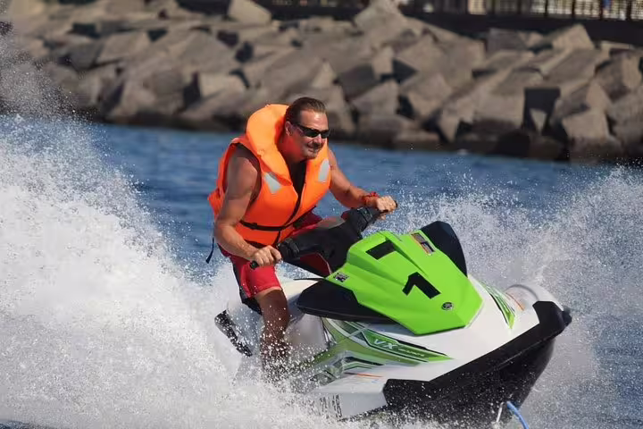 Man in orange life vest rides a jet ski with dynamic speed and power, creating splashes on a 2-hour safari tour.