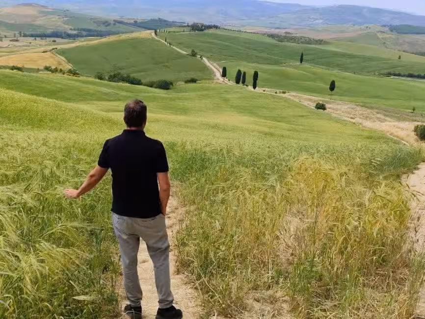 Man standing in a picturesque Tuscan landscape near Montepulciano, surrounded by rolling green hills.