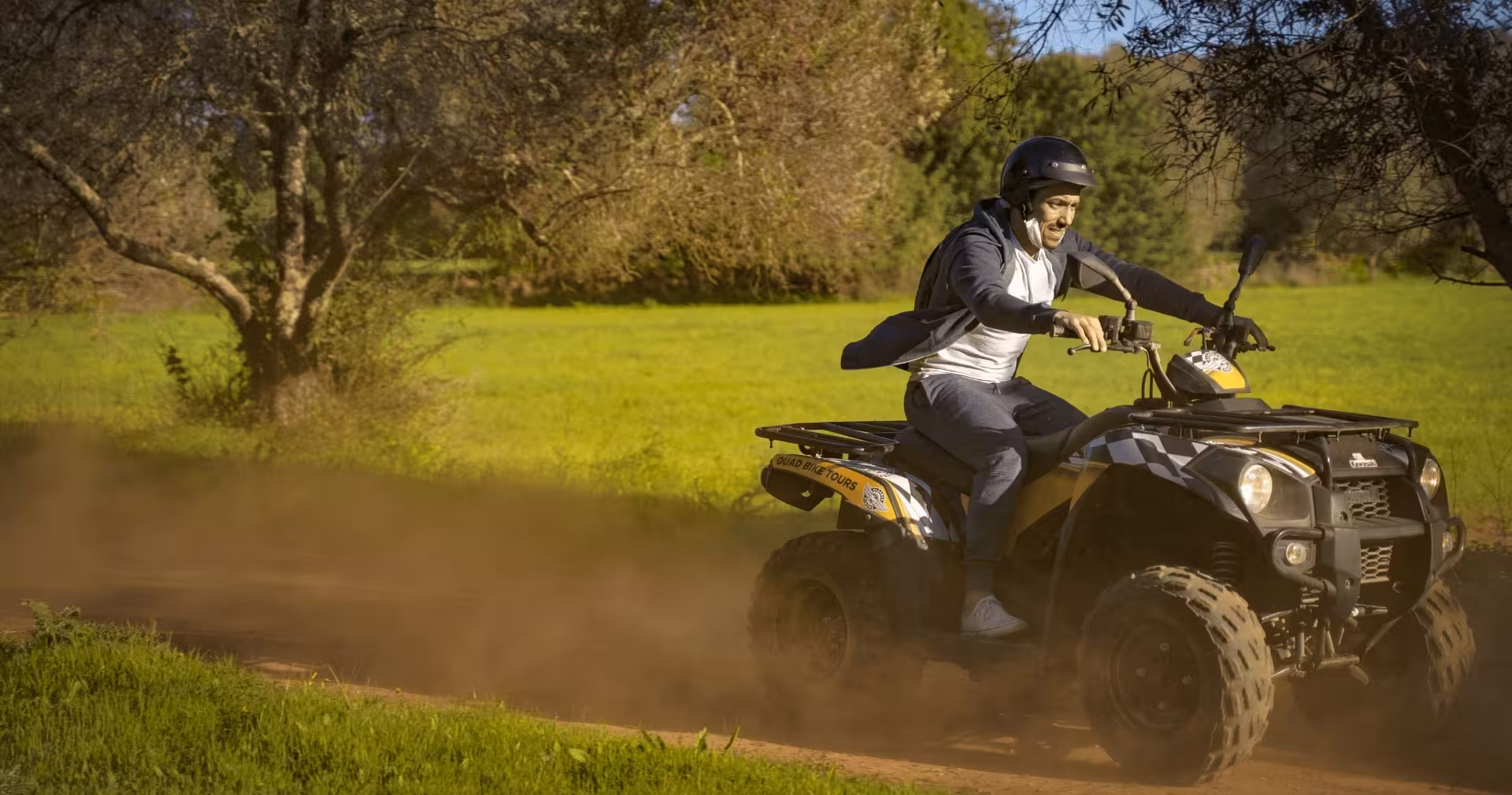 Smiling man speeds through a dusty forest trail on a quad bike during a guided half-day off-road ATV tour