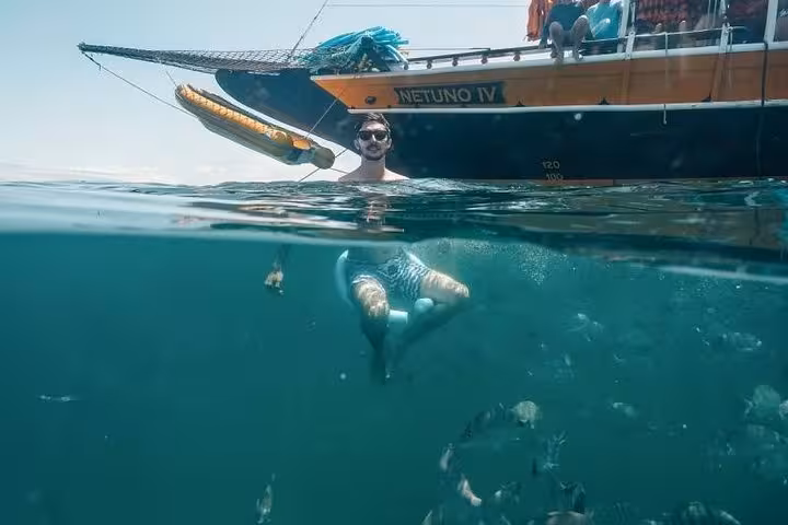 Man relaxing in the water near a boat, surrounded by fish, offering an immersive aquatic tour experience.