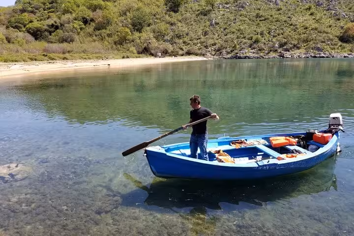 Man rowing a blue boat on the serene waters of Butrint National Park in Albania, surrounded by lush greenery.