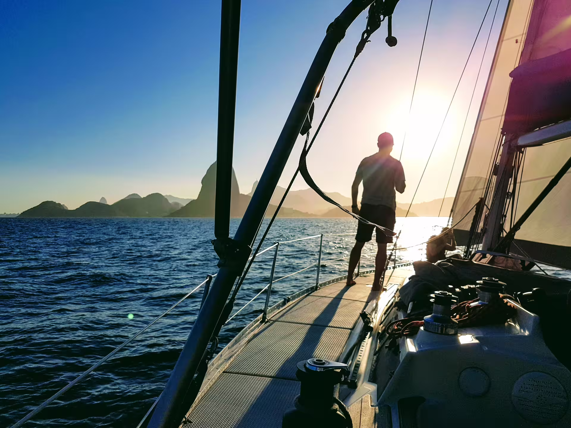 Man stands on a sailboat deck at sunrise, experiencing the beauty of a private sailing tour with KAMEHAMEHA.