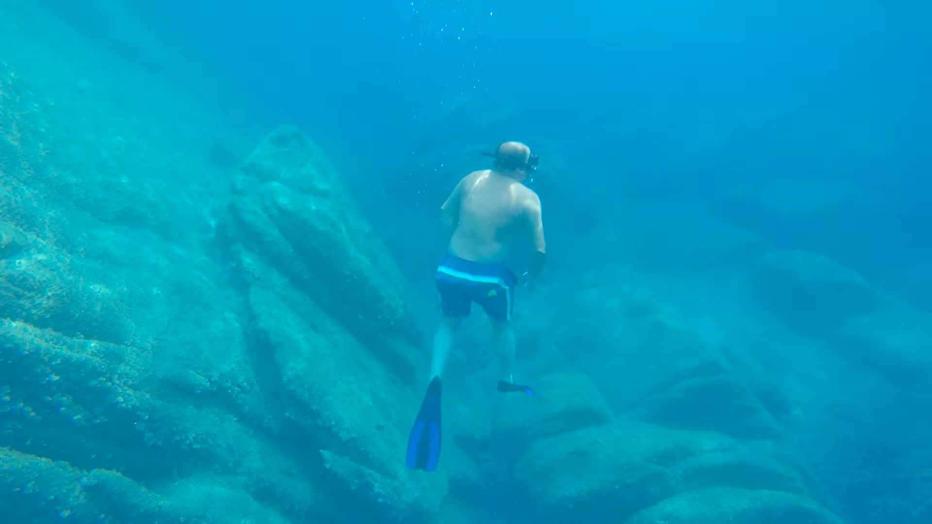 Man snorkelling in Porto Conte Park's clear blue waters, exploring underwater rock formations in Alghero.