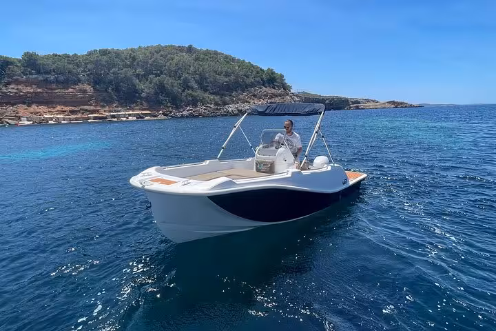 Man steering a boat off Ibiza's scenic coast, showcasing easy navigation without a boating license.