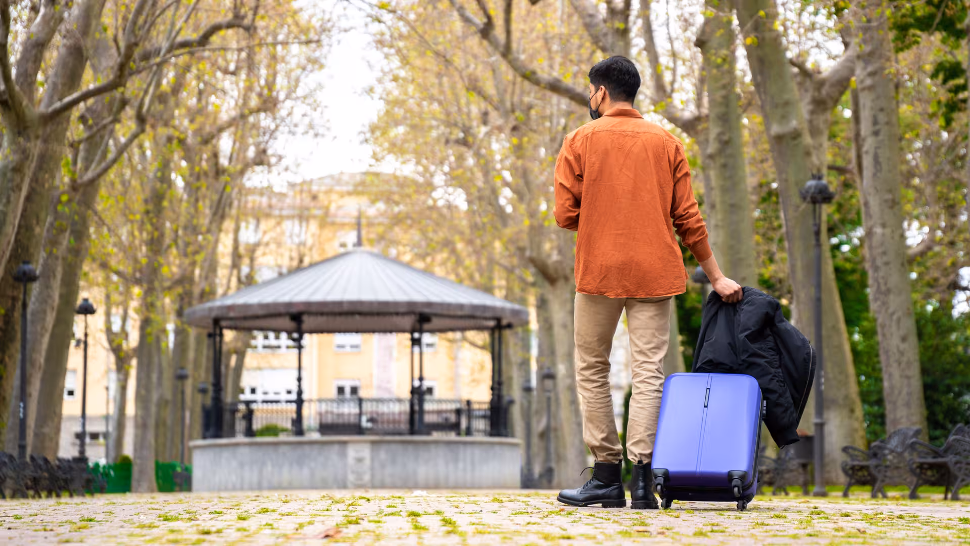 Man with rolling suitcase in park, using secure London luggage storage close to Kings Cross and Euston