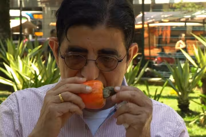 Man savoring the aroma of a fresh persimmon during a guided Rio tropical fruit tasting tour in a lush park.