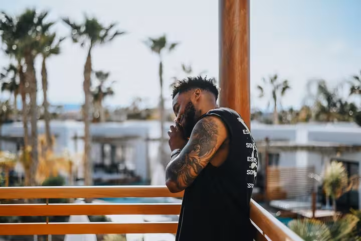Man with tattoos contemplating on a balcony overlooking tropical scenery, captured during a private Anisaras photoshoot.