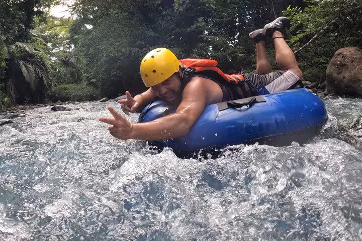 Excited man tubing down the rapids in Rio Celeste, showcasing adventure and thrill with safety gear.