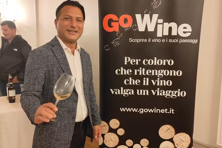 Man holding wine glass in front of GoWine banner at Rome wine education course event.