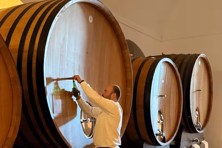 Man sampling wine from large wooden barrels in a cellar on the Alentejo Wines private tour.