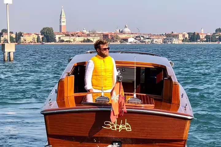 Man standing on a wooden boat in Venice with cityscape in the background during Grand Canal tour from San Marco.
