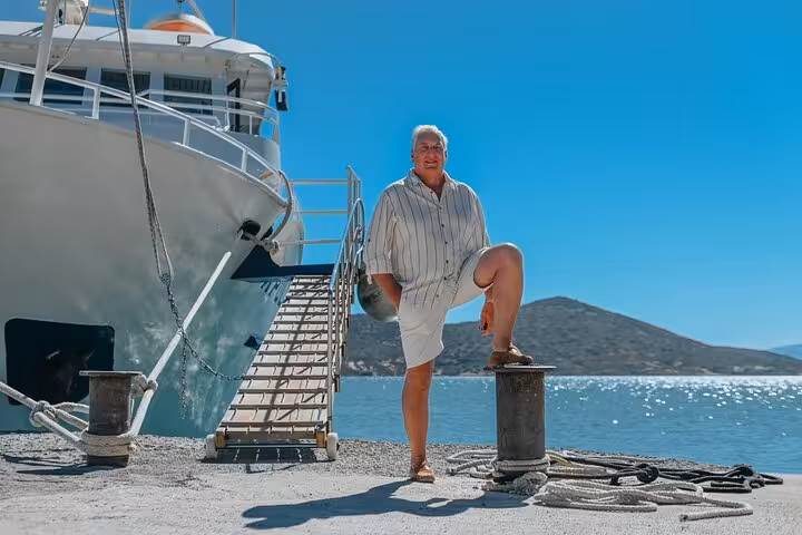 Man posing confidently by a docked yacht in Elounda under a clear blue sky.