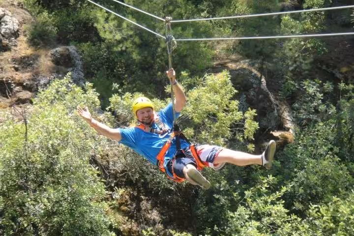 Man ziplining over green canyon with safety harness, included in great threesome rafting buggy zipline package