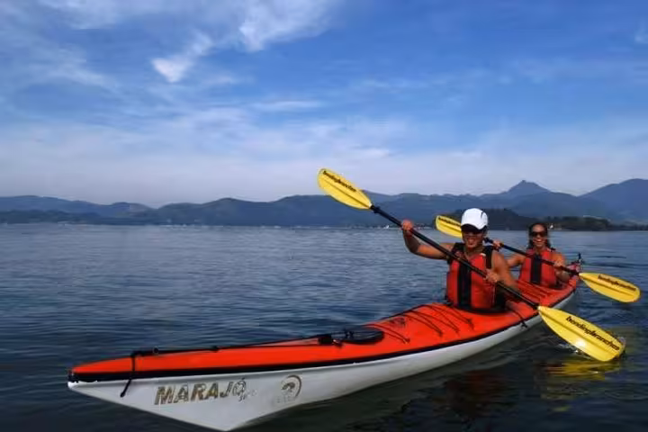 Two people kayaking with yellow paddles on a calm sea during the Mangrove and Beach Kayak Tour by Paraty Tours.