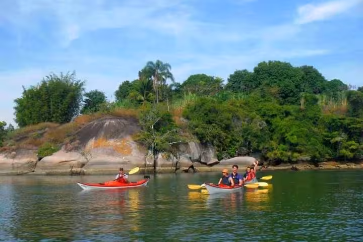 Group kayaking near lush green mangroves and rocky shores on the Mangrove and Beach Kayak Tour by Paraty Tours.