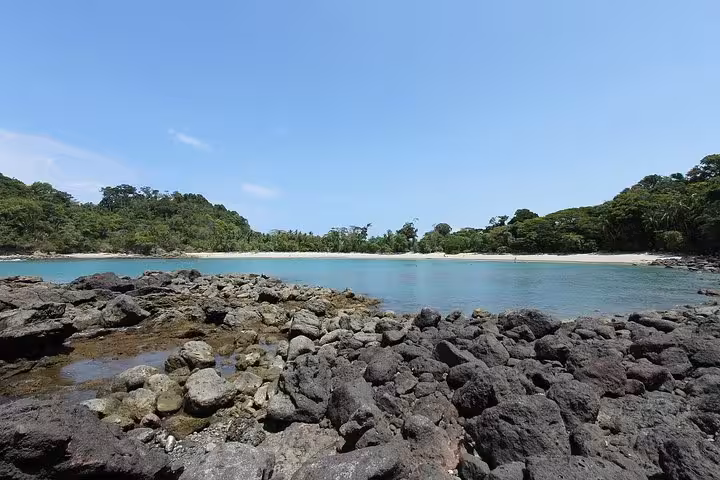 Scenic view of a serene beach with rocky foreground and turquoise waters at Manuel Antonio National Park.