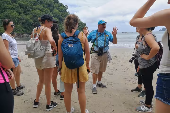 Tour group listening to a guide on the sandy beach of Manuel Antonio National Park, highlighting an engaging guided tour experience.
