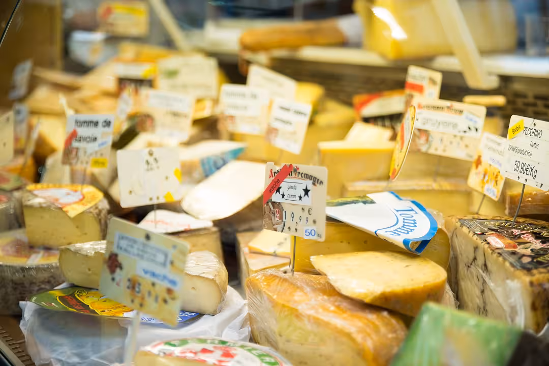 Variety of artisanal cheeses displayed with labels at a Marais District shop on a food walking tour.