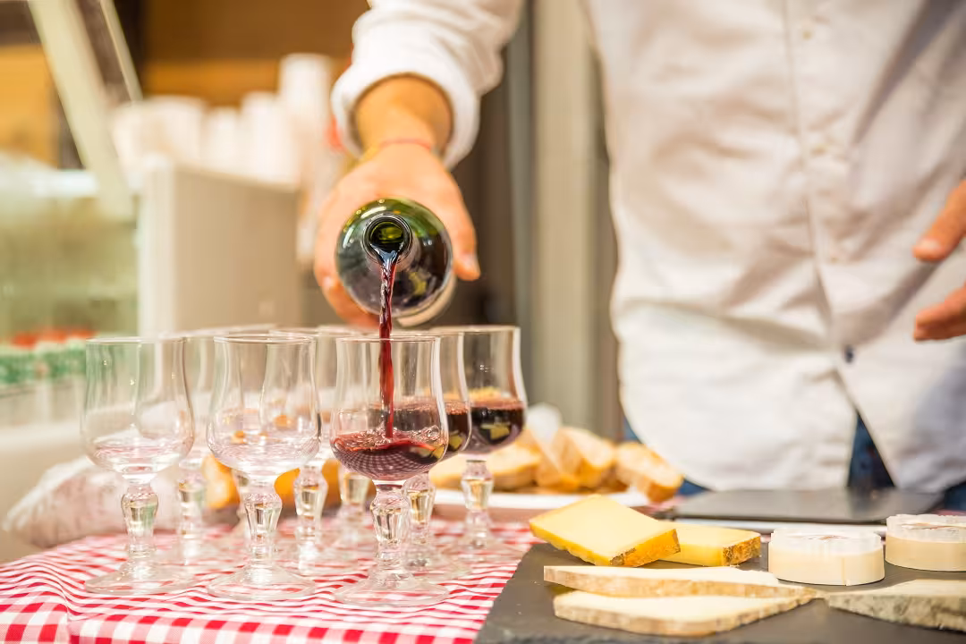 Pouring red wine into glasses surrounded by assorted cheeses on the Marais District walking tour.