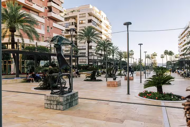 Modern plaza in Marbella adorned with sculptures and palm trees, offering a glimpse of local culture on a group tour.