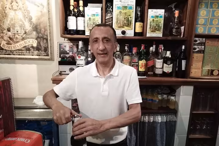 Friendly bartender opening a bottle in a cozy Marbella tapas bar, showcasing a variety of spirits.