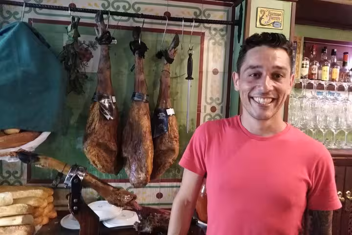 Smiling guide in front of hanging Iberian ham, showcasing local flavors on the Marbella Tapas Adventure.